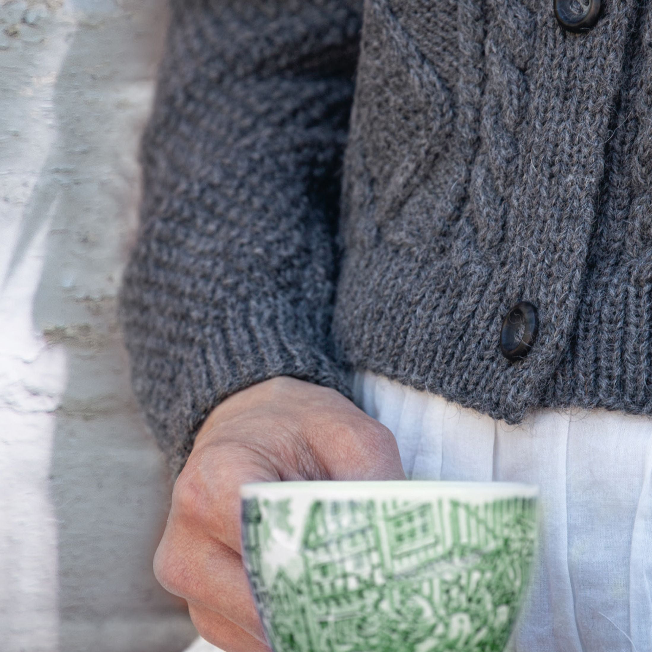 Neuleisiin pukeutunut nainen pitelemässä teekuppia kädessään